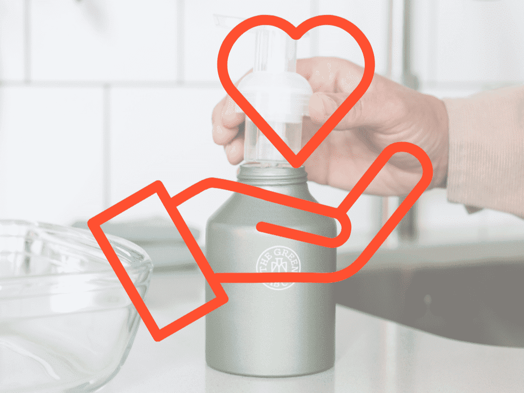 Hand using a reusable The Green Lab Co. pump bottle on a kitchen counter, with a red hand-and-heart icon overlay symbolizing care and sustainability.